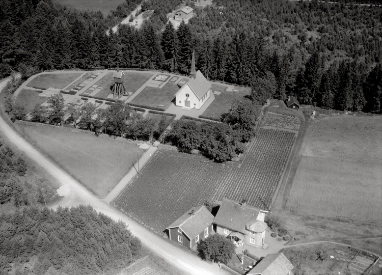 Svartvit flygbild över Fiskebäcks kapell, skog och åkermark.