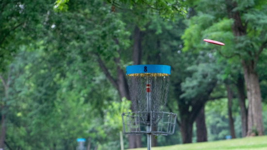 Frisbee som flyger mot ett discgolfskorg.