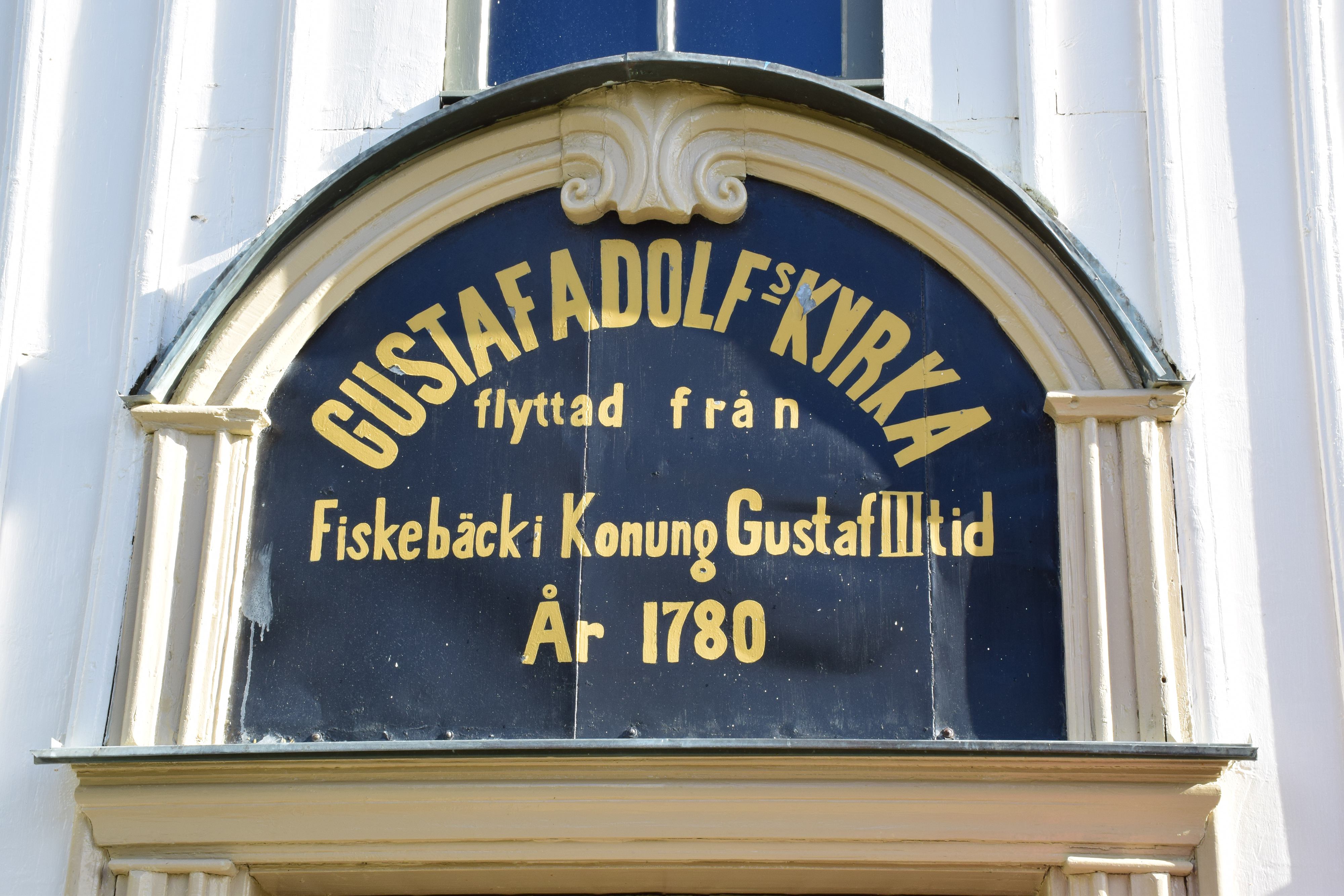 Text på en fasad där det står Gustaf Adolfs kyrka flyttad från Fiskebäck i Konung Gustaf III tid år 1780.