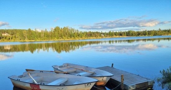 Två roddbåtar ligger vid en liten brygga i en sjö.