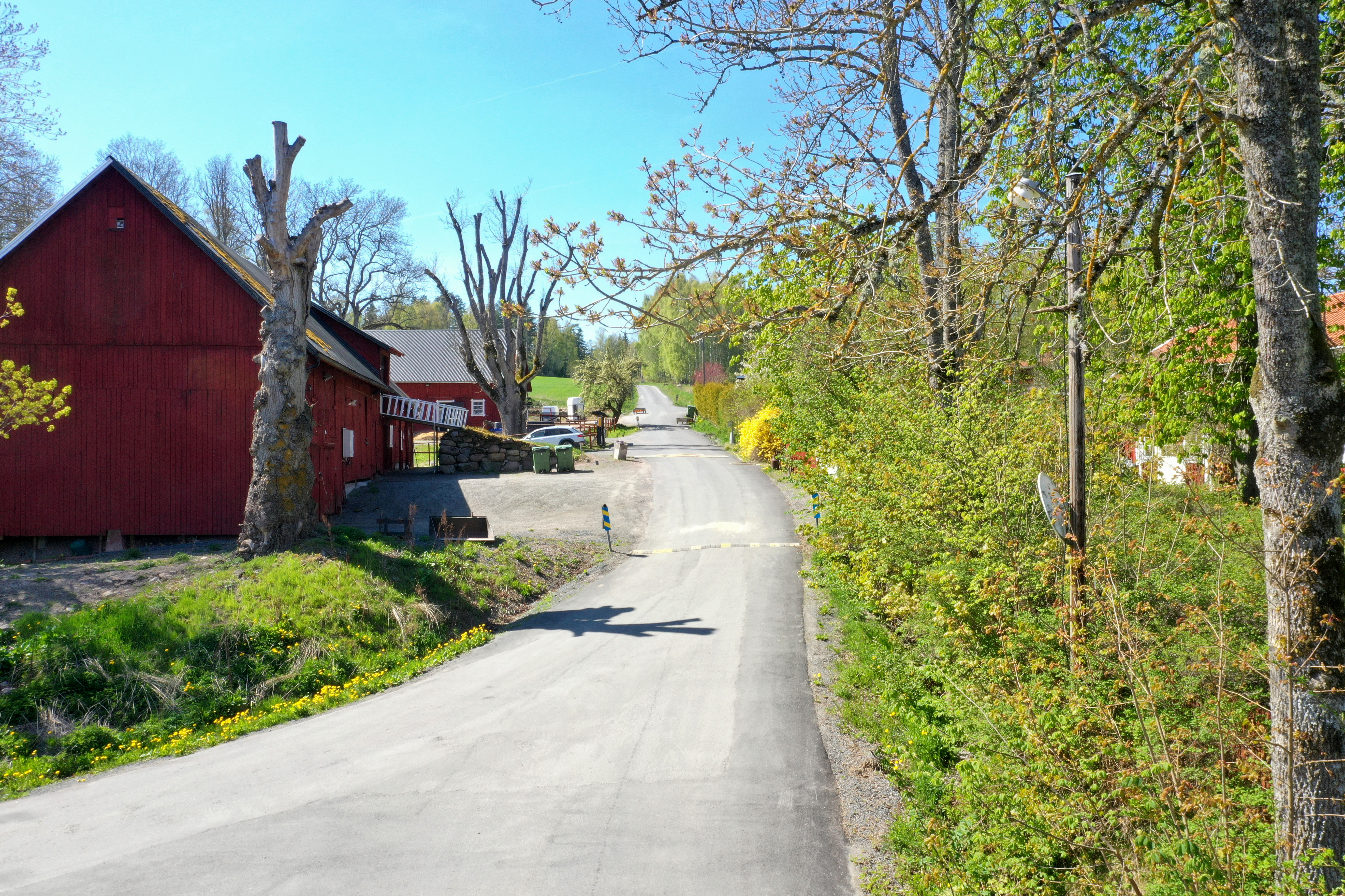 Liten lantlig väg med en röd gård på vänster sida.