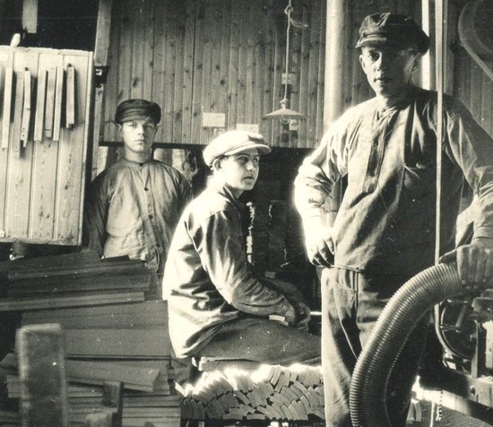 Gammal bild av tre unga män i en fabrik.