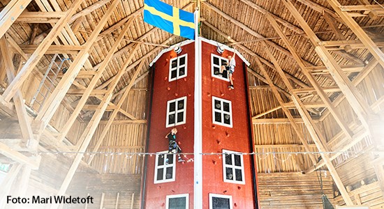 En röd klättervägg inuti en lada som två pojkar klättrar upp för.