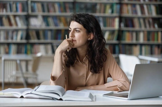 Tjej i bibliotek med  dator och böcker.