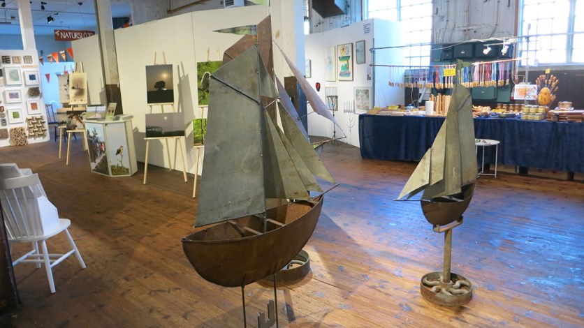 Konstfesten 2021, segelbåtar i metall framför utställda tavlor, foton och slöjdade föremål