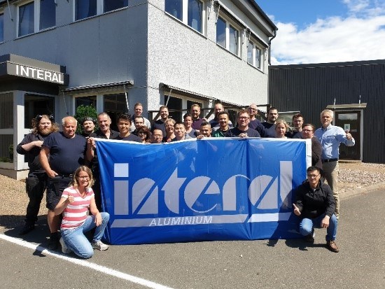 Personalen på Interal står framför fabriken med en blå flagga där det står Interal.